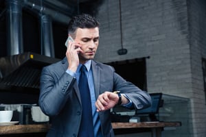 Confident businessman speaking on the phone and looking on the wristwatch in cafe-1