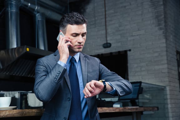 Confident businessman speaking on the phone and looking on the wristwatch in cafe-1