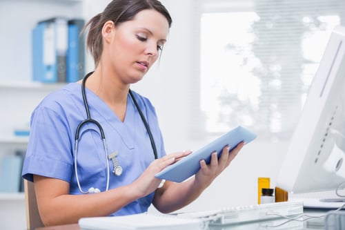 Side view of young female surgeon using digital tablet in front of computer at desk in clinic Side view of young female surgeon using digital tablet in front of computer at desk in clinic