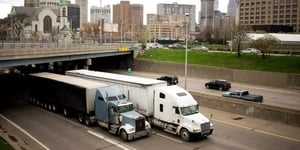 Two semi trucks driving on highway under urban overpass