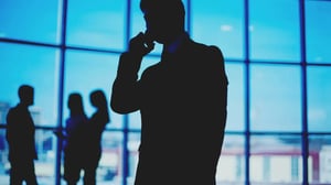 Silhouetted businessman on a phone call near large windows.