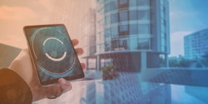 Hand holding a tablet with smart connectivity interface in front of a hotel