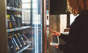 Woman using vending machine with phone in hand.
